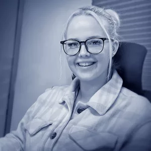 Céline Stoltenberg an ihrem Arbeitsplatz im Qualitätsmanagement der W&W Personaleinsatz GmbH, von wo aus sie auch die Kundenberatung im Backoffice unterstützt. Sie blickt lächelnd in die Kamera.