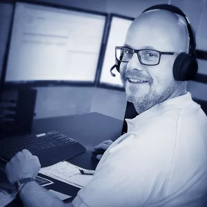 Stefan Wylega sitzt vor seinen Monitoren, Tastatur und Notizen in der Kundenberatung der W&W Personaleinsatz GmbH. Mit Telefon-Headset auf dem Kopf unterbricht er kurz seine Arbeit, blickt über seine Schulter nach hinten und lächelt freundlich.