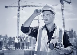 Ein Bauarbeiter mit Schutzbrille, Helm, Ohrenschützern und Warnweste setzt den Arbeitsschutz vorbildlich um.